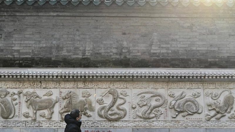 Мужчина рассматривает изображение змеи на каменной стене, посвящённое китайскому зодиаку, во время посещения даосского храма Байюнь, также известного как Храм Белого Облака, в Пекине 23 января 2025 года. Фото: Педро Пардо | Epoch Times Media