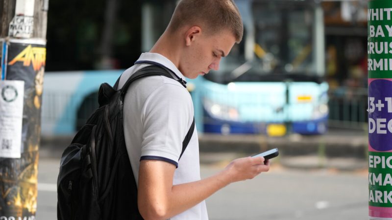 На снимке запечатлен подросток, использующий свой телефон, пока он ждет, чтобы перейти улицу в Сиднее, 8 декабря 2025 года. (AP Photo/Rick Rycroft)
