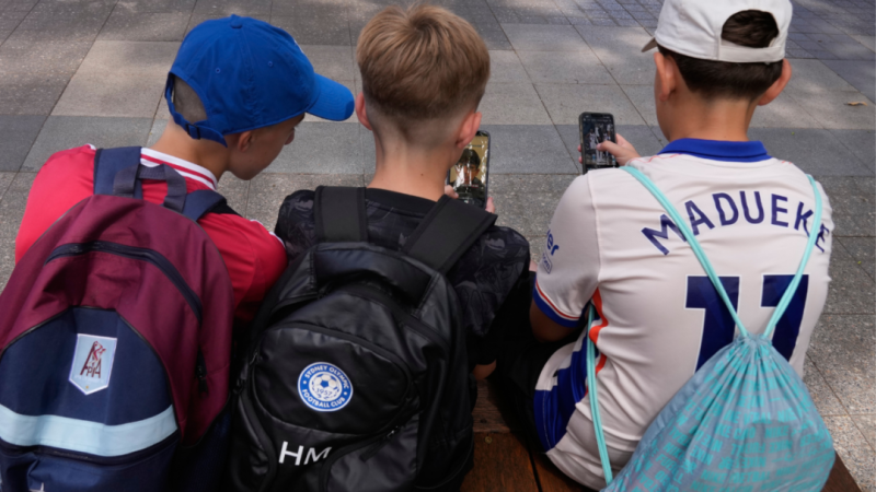 Трое 11-летних мальчиков пользуются телефонами, сидя на улице возле школы в Сиднее, Австралия, 8 декабря 2025 года. (Фото Рика Райкрофта, AP) | Epoch Times Media