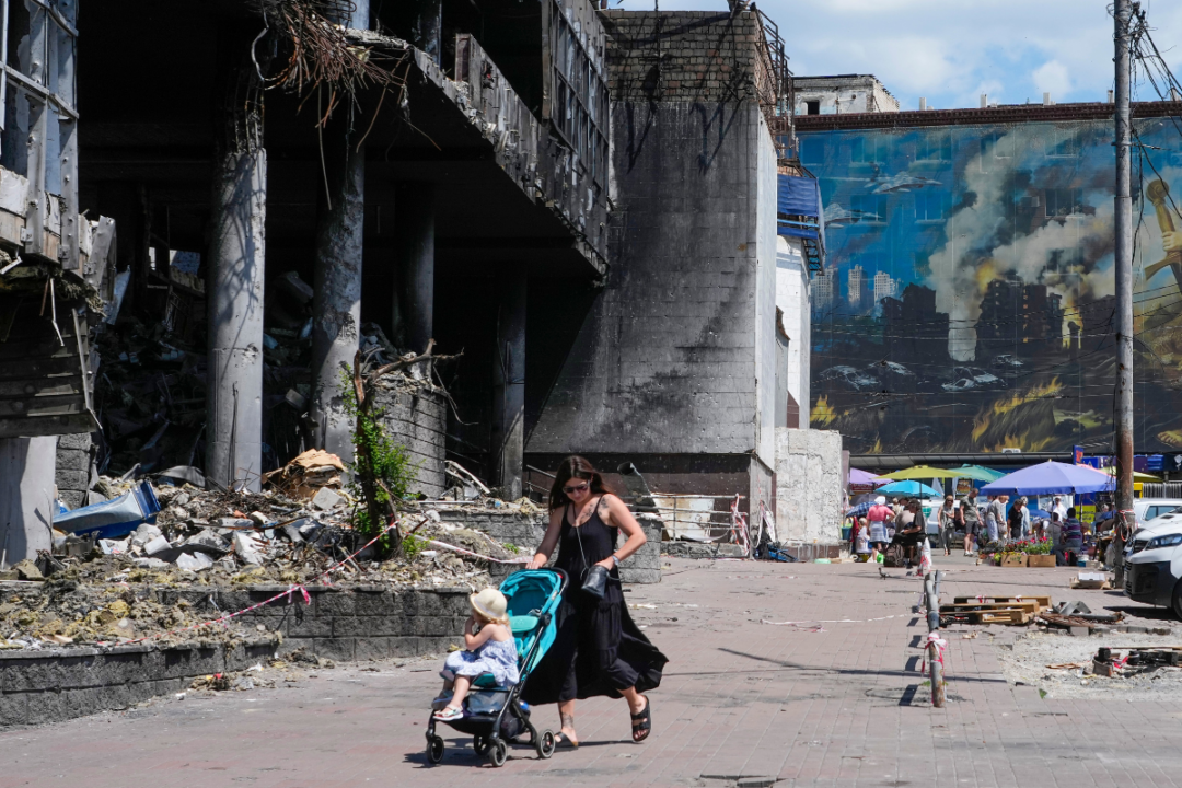 22 июня 2026 года в Киеве (Украина) мать толкает детскую коляску мимо поврежденного здания, покрытого рисунками уличных художников, и большого городского рынка, недавно разрушенного российскими ракетами. (Эфрем Лукацкий/ AP Photo) | Epoch Times Media