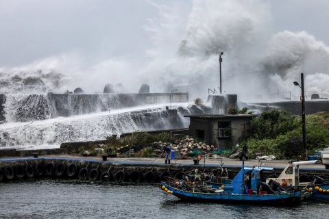 Рыбак держит веревку возле рыболовной лодки, в то время как волны перехлестывают волнорез, когда тайфун Бави движется в сторону северо-восточного Тайваня, Илань, Тайвань, 10 июля 2026 года. (I-Hwa Cheng / AFP via Getty Images) | Epoch Times Media