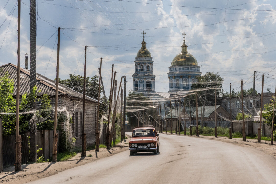 22 июля 2026 года в Изюме (Украина) автомобиль движется по дороге, защищённой сетками от дронов, на фоне собора Вознесения Господня. (Роман Пилипей/AFP via Getty Images) | Epoch Times Media