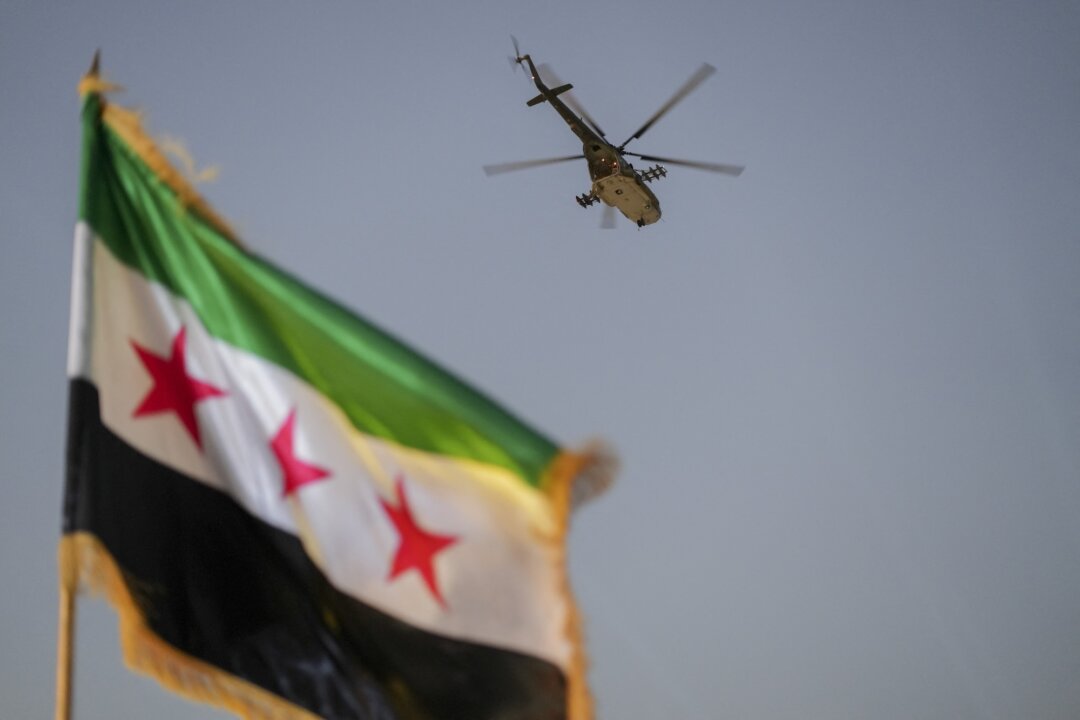 Военный вертолет пролетает над сирийским флагом в Дамаске, Сирия, 9 августа 2026 года. (Омар Альбам/Middle East Images via AFP/Getty Images) | Epoch Times Media