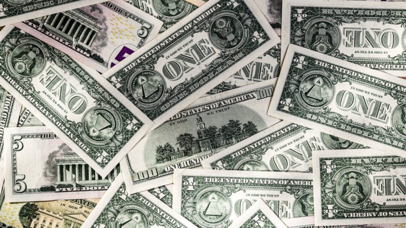 Разбросанная куча различных долларовых купюр: номиналом 1, 5, 20 и 100 долларов.
